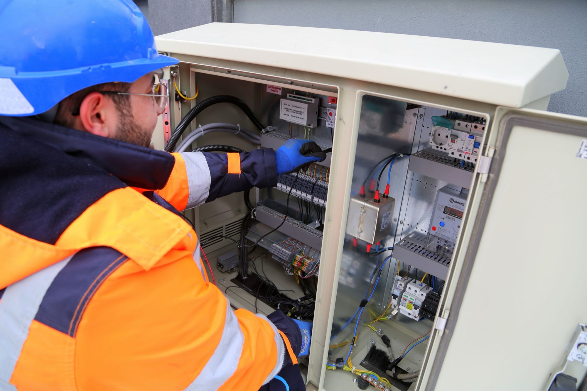 A technician in a hard hat and hi-vis jacket wiring an outdoor equipment cabinet. Illustrative photograph.