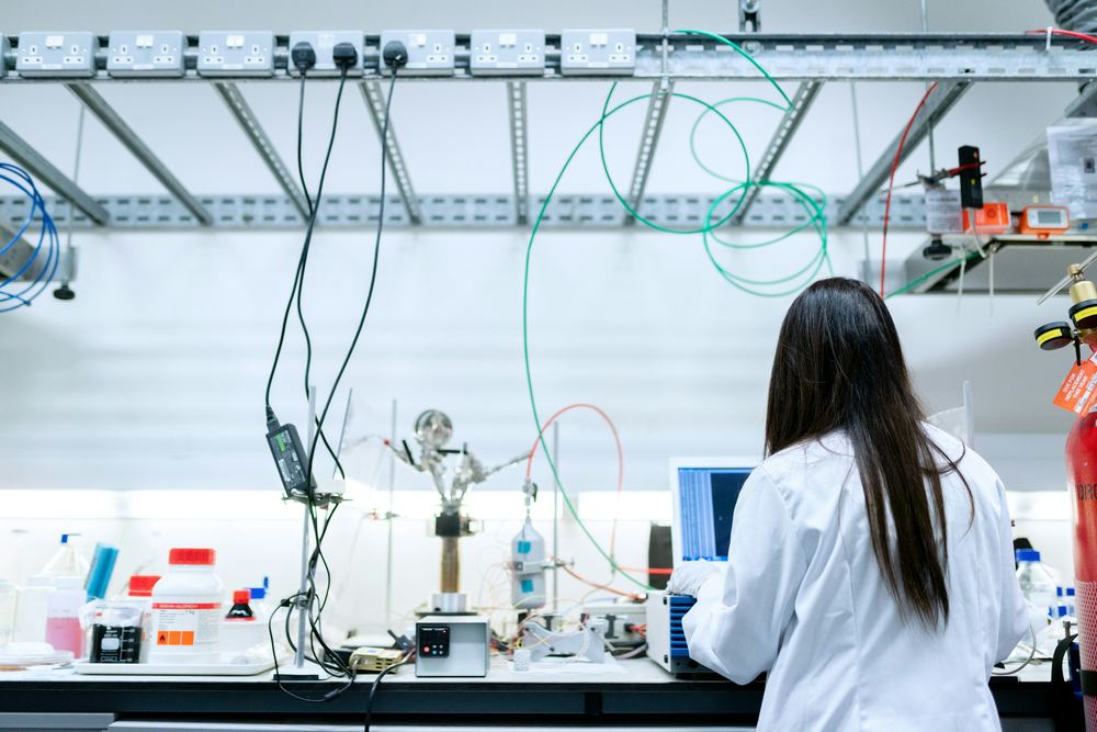 A researcher at a laboratory bench with instruments and a laptop.